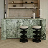 Two black sculptural bar stools with cream round cushions beside a green marble-patterned kitchen island.