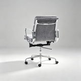 A modern office chair with a gray textured fabric upholstered seat and backrest, supported by a polished chrome five-star base with dual-wheel casters, photographed from a rear three-quarter angle against a neutral light gray studio background.