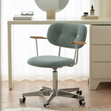 Light blue boucle office chair with wooden arm pads and a polished castor base beside a white dressing table.