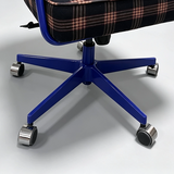 Close-up of an office chair base with a blue five-star metal frame and silver caster wheels, paired with a black and pink plaid upholstered seat cushion.