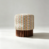 A cylindrical upholstered stool with a cream fabric top featuring multicolored vertical dotted stripes and a fluted dark brown wooden base, photographed on a light gray studio background.
