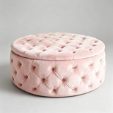 A round, tufted velvet ottoman stool in a soft light pink color, shown against a neutral light gray studio background.