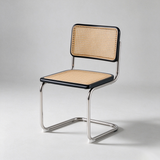 A modern cantilever dining chair with a black metal frame, a natural cane seat and backrest, and a light gray studio background.