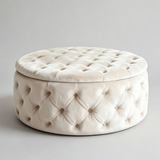 A round tufted ottoman stool in a warm cream velvet fabric, featuring a padded lid and decorative button tufting, set against a neutral light gray background.