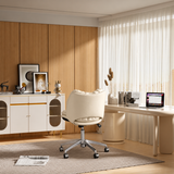 Cream swivel office chair viewed from behind at a curved desk beside sheer curtains and a white storage cabinet.
