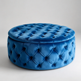 A round tufted velvet ottoman stool in a rich royal blue color, photographed against a neutral light gray studio background.