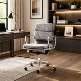 A modern gray fabric office chair with a chrome metal base and armrests, positioned in a styled home office environment with a desk, lamp, and wooden shelving.