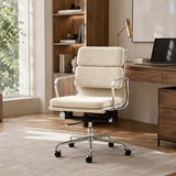 A modern upholstered office chair in a warm cream fabric with chrome metal armrests and a five-wheel base, positioned in a bright, contemporary home office next to a wooden desk and bookshelf.