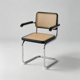 A modern cantilever dining chair with a black frame, polished chrome legs, and a natural cane seat and backrest, photographed on a light gray studio background.