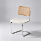 A modern dining chair with a tufted cream seat, a natural woven cane backrest, and a curved chrome metal frame, photographed on a light gray studio background.
