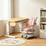 A children's desk and matching ergonomic chair set in a bright, modern room. The desk has a light wood top and white frame, while the chair features a pink seat and back with gray and white accents.