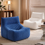 A blue ribbed fabric lounge chair in the foreground, with a white matching lounge chair behind it in a softly styled living room setting.