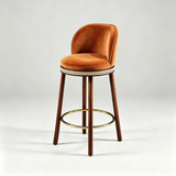Orange Alma bar stool with a curved upholstered backrest, dark wood legs and a gold-tone circular footrest.
