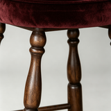 Close-up of the stool's turned brown wooden legs and visible grain beneath the burgundy upholstered seat.