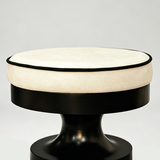 Close-up of the cream round seat cushion with black piping above the black wooden stool frame.