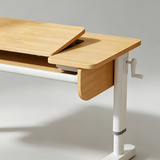 Close-up of a wooden desk with a light natural wood finish and a white metal leg, showing a crank handle and a lift-top section.