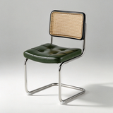 A modern side chair with a dark green tufted leather seat, a black-framed cane backrest, and a chrome cantilever metal base, shown on a light gray studio background.