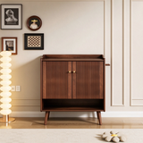Walnut-finish shoe cabinet beside a dining chair, topped with a leafy vase, shallow bowl and two wooden mills.
