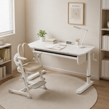 A white adjustable height desk with a matching beige ergonomic chair, styled in a bright, minimalist home office setting with a round beige rug, wooden floor, and bookshelves.
