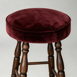 Close-up of the burgundy round seat cushion with piped edging above the stool's turned wooden frame.