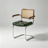 A modern accent chair with a dark green tufted leather seat, a woven cane backrest, dark brown wooden armrests and frame, and a chrome cantilever steel base, photographed on a light gray studio background.