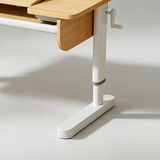 Close-up of a height-adjustable desk showing a light wood tabletop, white metal leg with a hand crank, and gray adjustment band on a light gray studio background.