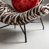 Close-up of the lounge chair's curved zebra-print seat edge, black metal support frame and angled legs.
