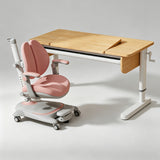 A children's ergonomic desk and chair set on a light gray studio background. The desk has a light natural wood top and white frame, with a matching adjustable pink and gray ergonomic chair positioned in front.