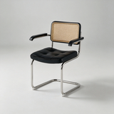 A modern cantilever chair with a black tufted leather seat and black armrests, featuring a woven cane backrest and a chrome steel base, photographed on a light gray studio background.