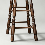 Close-up of the bar stool's turned wooden legs, horizontal footrest rails and rounded feet.
