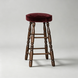 Dark brown wooden bar stool with a burgundy upholstered round seat, turned legs and wooden footrest rails.