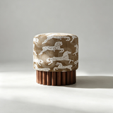 A cylindrical upholstered stool or ottoman with a brown and white animal-patterned fabric top and a fluted dark wood pedestal base, photographed against a light gray studio background.