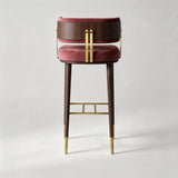 A modern bar stool featuring a deep burgundy velvet cushioned seat and backrest, dark brown wood side panels, and polished gold metal hardware and leg caps, shown against a neutral light gray background.
