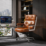 Cognac tufted office chair with silver arm supports and a castor base beside a desk and dark shelving.