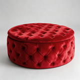 A round red velvet ottoman with a tufted button design, shown on a light gray studio background.
