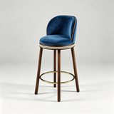 Blue Alma bar stool with a curved upholstered backrest, dark wood legs and a gold-tone circular footrest.
