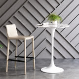 Round bar table with a grey-veined white top and white pedestal base, paired with a cream bar stool.
