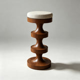 Warm brown wooden bar stool with a cream textured round cushion and a stacked hourglass-shaped pedestal base.