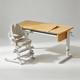 A modern adjustable height desk with a light natural wood top and white frame, paired with a matching ergonomic chair in a clean studio setting.