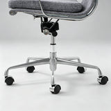 Close-up of an office chair base with a gray upholstered seat, chrome metal frame, and black caster wheels on a light gray studio background.