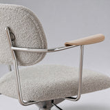 Close-up of the office chair's curved wooden arm pad, polished metal supports and light grey boucle upholstery.