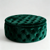 A round tufted velvet ottoman stool in deep emerald green, shown from a three-quarter angle on a light gray studio background.
