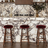 Three burgundy-cushioned wooden bar stools lined up beside a white kitchen island with dramatic dark veining.
