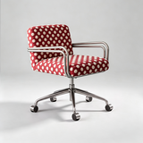 A modern office chair with a red and white polka-dot upholstered seat and backrest, supported by a chrome five-star base with casters, photographed on a light gray studio background.