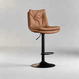 Camel bar stool with a button-tufted backrest, padded seat, black pedestal base and oval footrest.