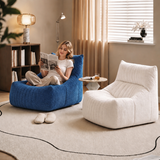A woman sits in a blue beanbag chair reading a magazine in a cozy, modern living room setting, next to a white ribbed lounge chair.