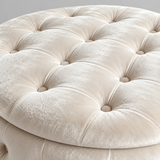 Close-up of a round tufted ottoman upholstered in cream velvet fabric, showing the button tufting and soft texture.