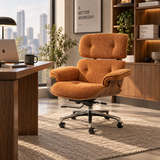 An orange-brown upholstered office chair with a tufted backrest and five-wheel base, placed in a modern home office setting next to a wooden desk.