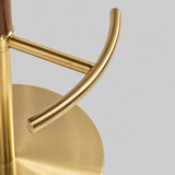 Close-up of the bar stool's curved gold-tone footrest, central pedestal and round brushed gold-tone base.
