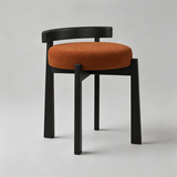 A modern dining chair with a black wooden frame and a round rust-orange upholstered seat cushion, photographed on a neutral light gray studio background.